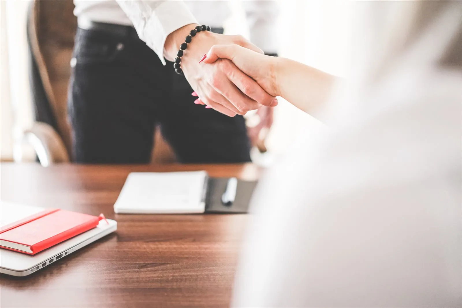 Two business professionals shake hands across a desk to seal a consulting agreement